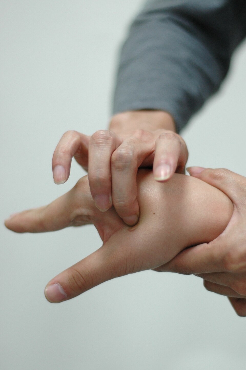 A person using their fingers to press a point on the back of another person's hand, possibly practicing acupressure or massage therapy, against a plain light background.